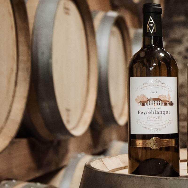 bouteille de 75 cl de vin blanc Graves Château Peyreblanque au milieu de tonneaux